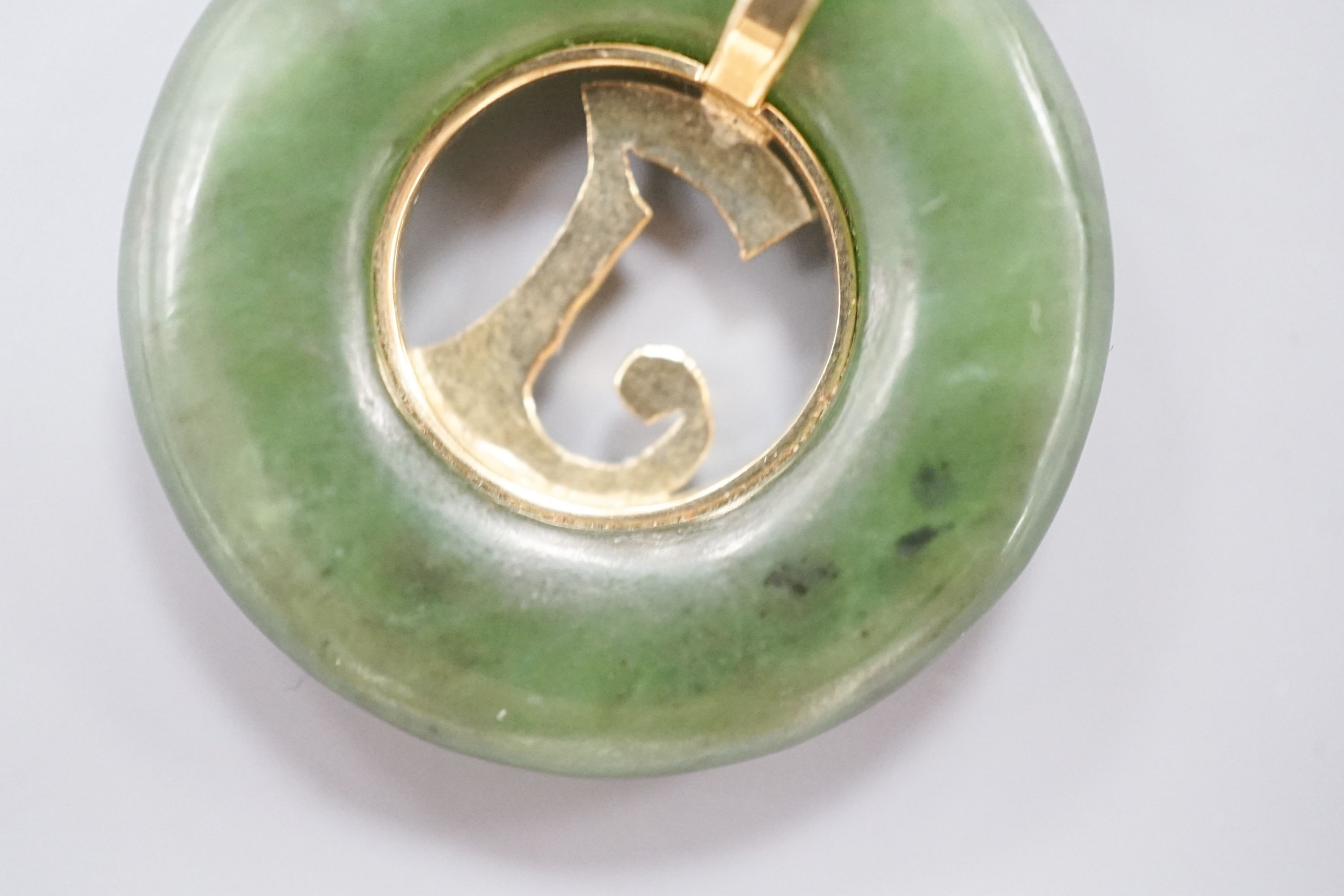 A yellow metal mounted pierced circular nephrite pendant, diameter 29mm, gross weight 8.5 grams.
